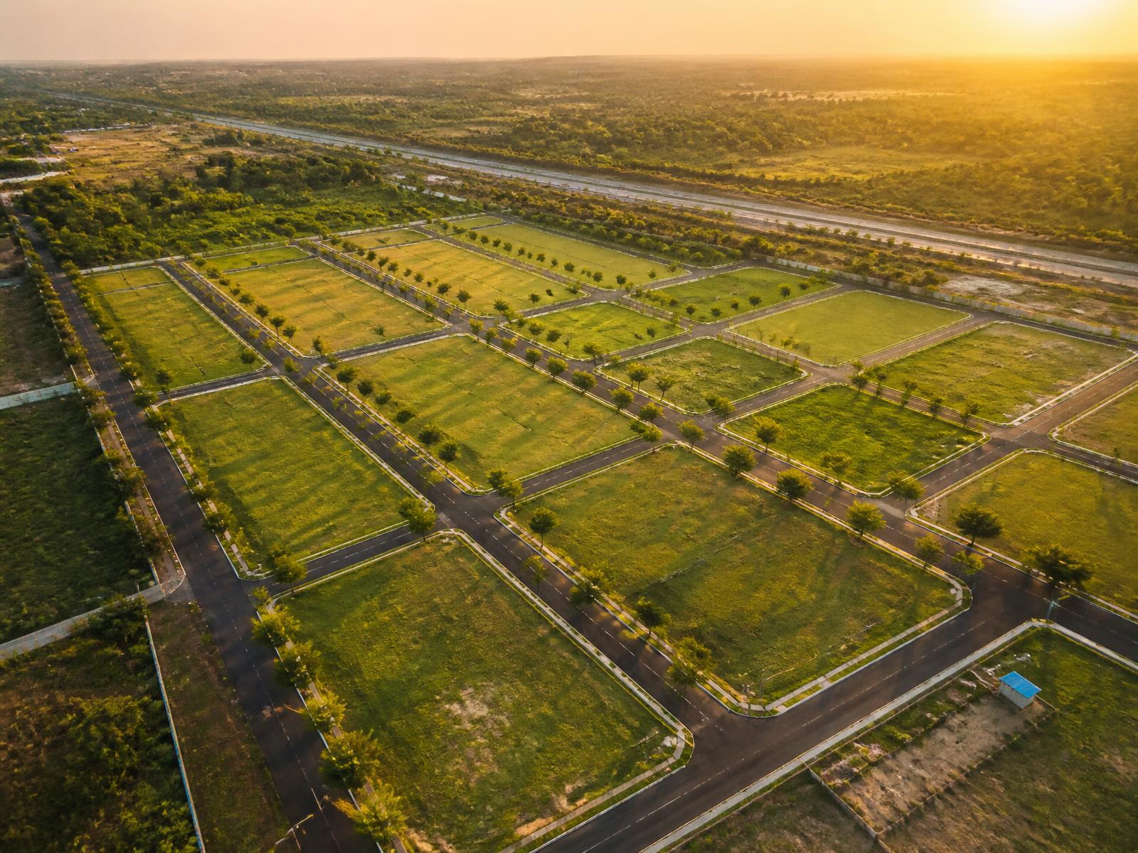 Aerial view of a surveyed open plot layout with black top roads and avenue plantation